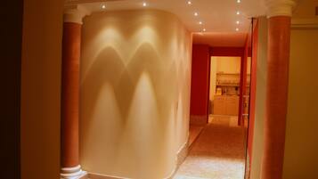 A corridor with columns, a curved wall, and a door leading to a room with a sink and cabinets.