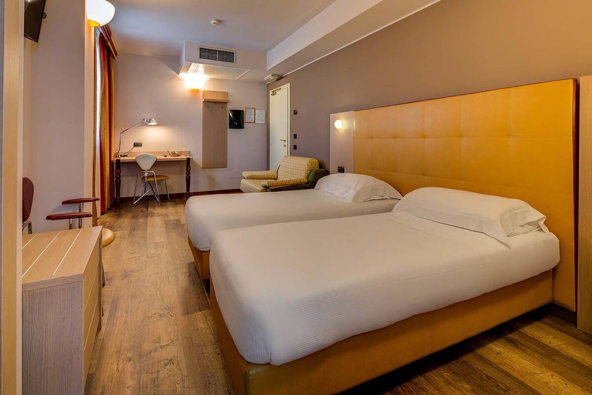 Habitación de hotel con dos camas, un escritorio, una silla y una pequeña kitchenette.