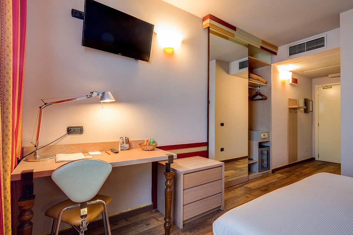 Una habitación de hotel con cama, escritorio, silla, televisor y armario.