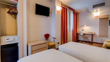 A hotel room with two beds, a desk with a chair, a TV, a wardrobe, and a bathroom.
