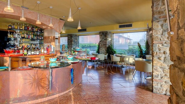 Una zona de bar con una barra curva, varias lámparas colgantes y una pared de piedra.