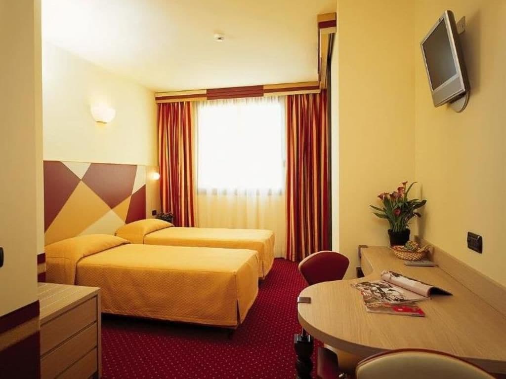 Camera d'albergo con due letti, una scrivania, una sedia, una televisione e una finestra con tende.