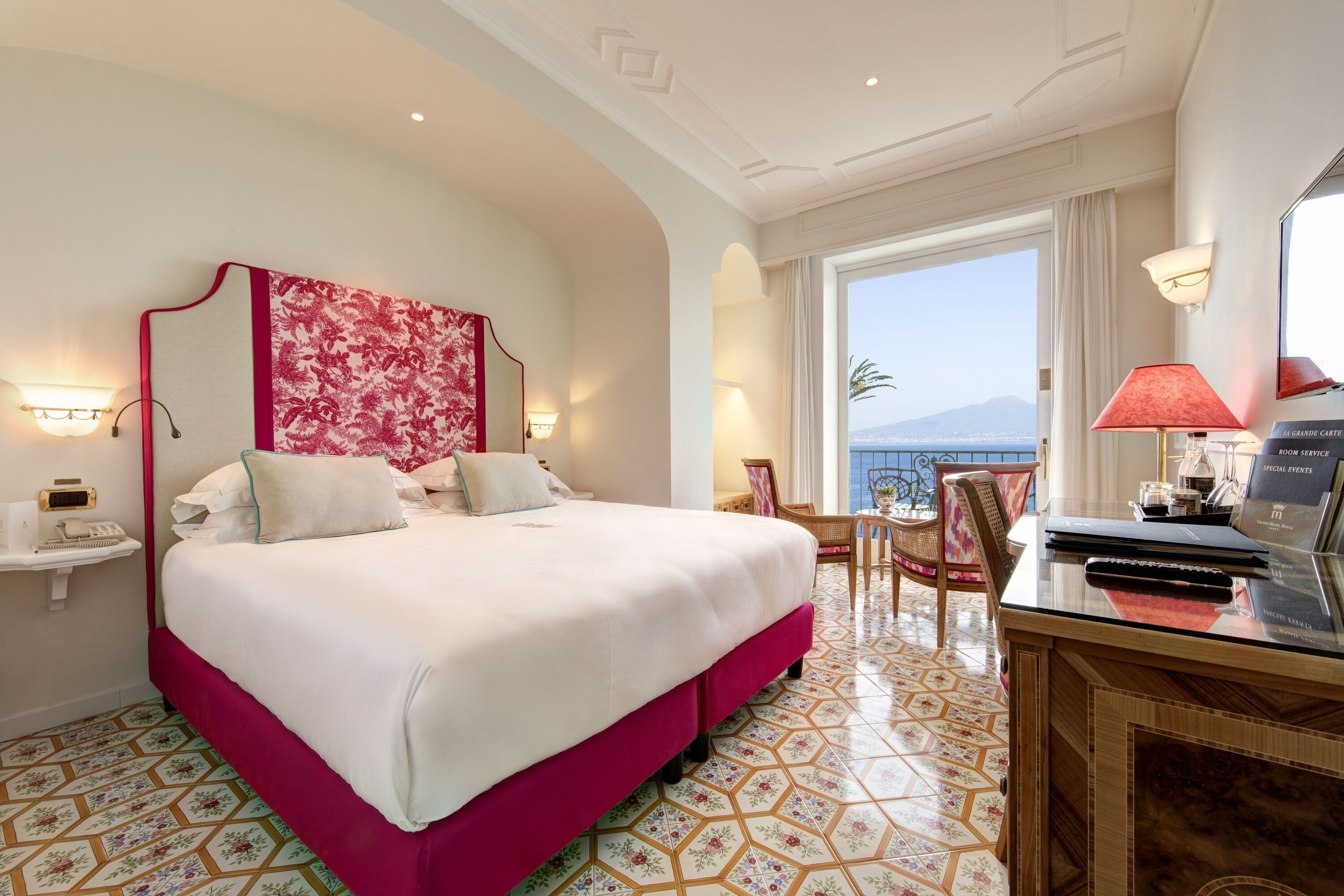 Habitación de hotel con una cama grande, un escritorio con una computadora portátil, una silla, vista al mar y un adorno en la pared.