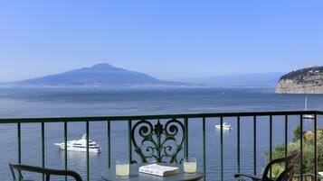 Ein Balkon mit Meerblick, ein Stuhl, ein Tisch mit einem Buch und Gläsern sowie eine ferne Berglandschaft.