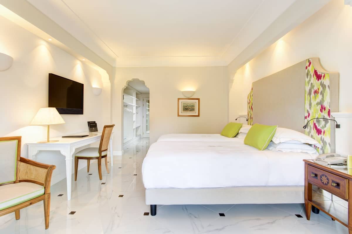 Habitación de hotel con cama, escritorio, silla, televisor y un cuadro en la pared.