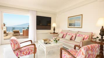 Habitación de hotel con balcón, sofá, dos sillones, una mesita de centro y televisor.