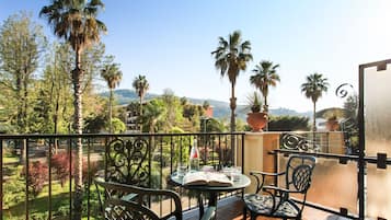 Un balcone con tavolo e sedie, affacciato su un giardino con palme e vista su colline lontane.