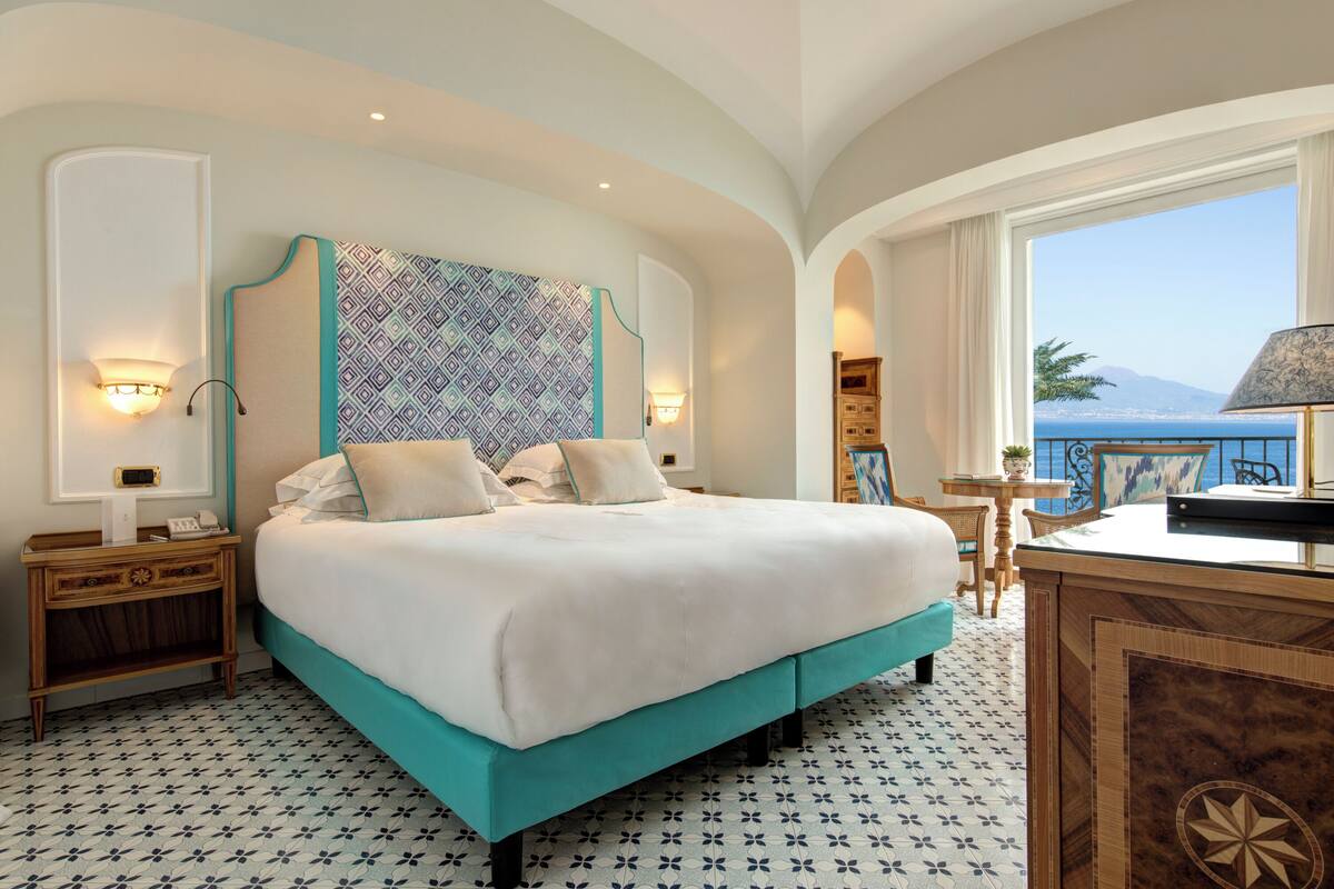 Habitación de hotel con una cama grande, vistas al mar y un pequeño balcón con mesa y sillas.