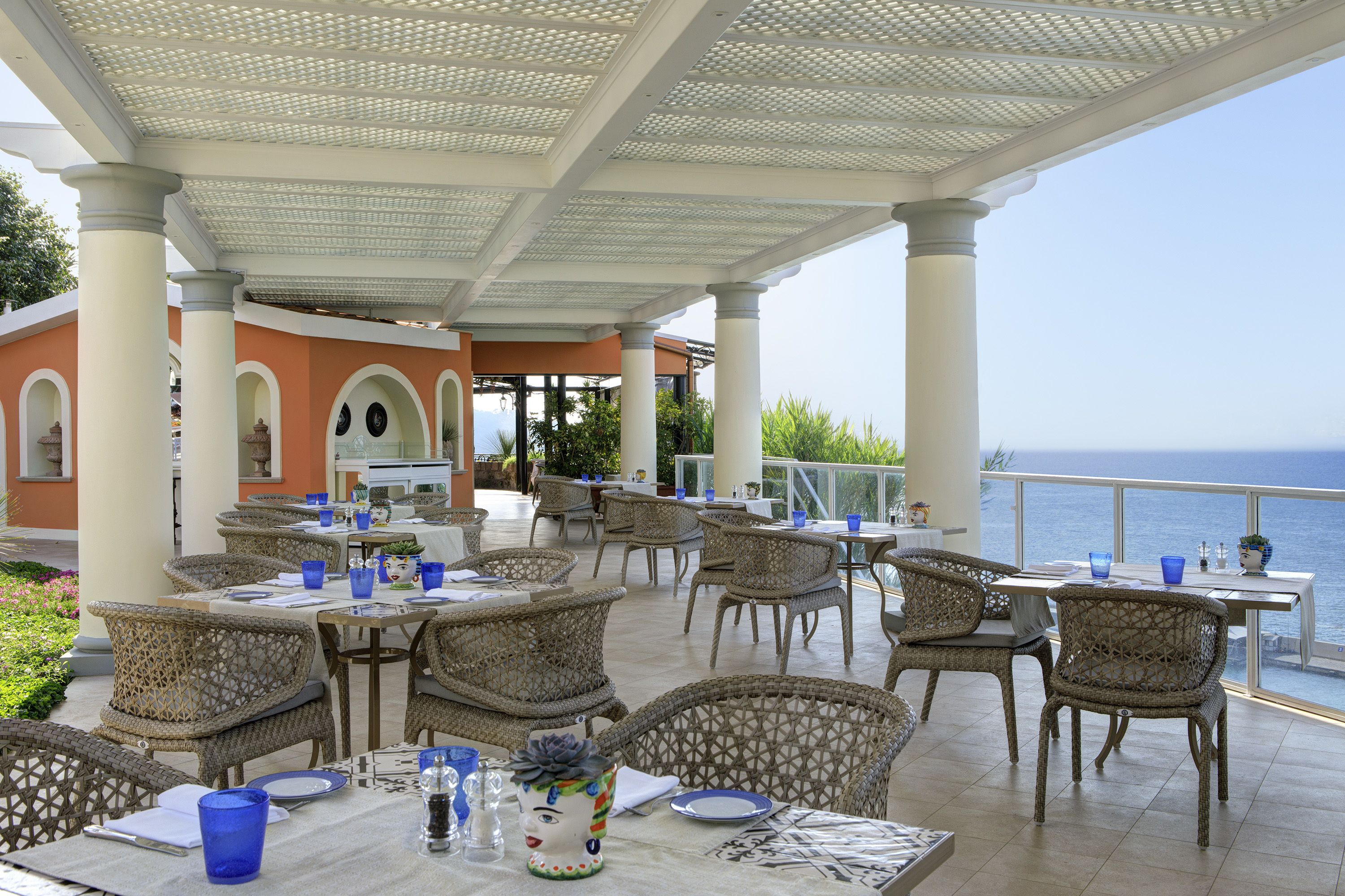 An outdoor dining area with wicker chairs and tables, overlooking the sea.