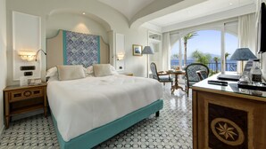 A hotel room with a large bed, a desk with a chair, a TV, and a view of the sea. - Grand Hotel Royal (Sorrento)