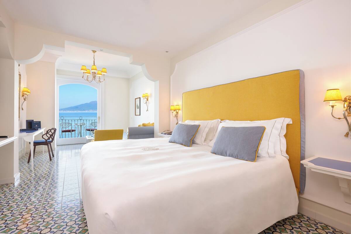 Een hotelkamer met een groot bed, een bureau en uitzicht op zee.