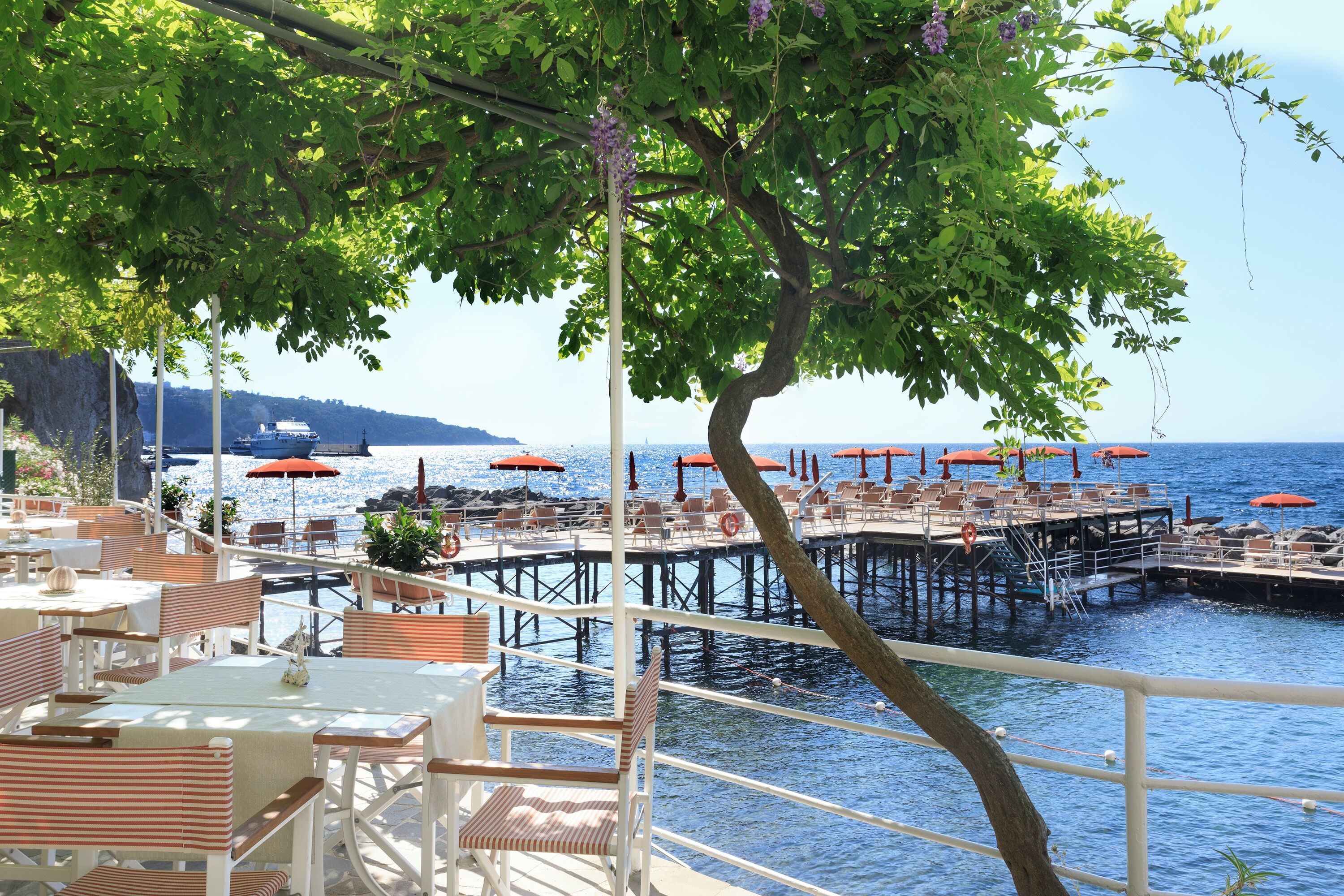 An outdoor dining area with tables and chairs, overlooking a pier extending into the water.