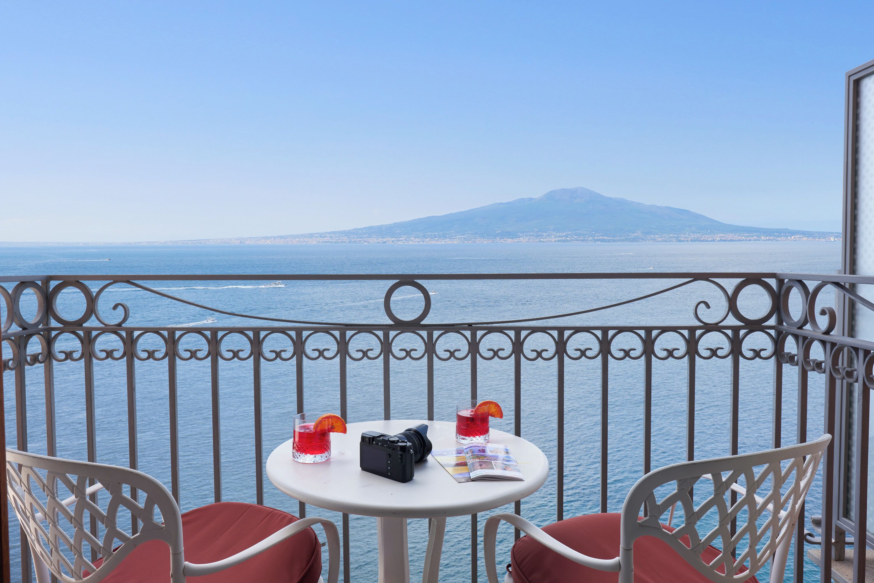 Un balcone con tavolo e sedie, affacciato su un corso d'acqua e una montagna in lontananza.