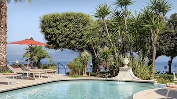Una piscina al aire libre, sombrillas, sillones reclinables de piscina