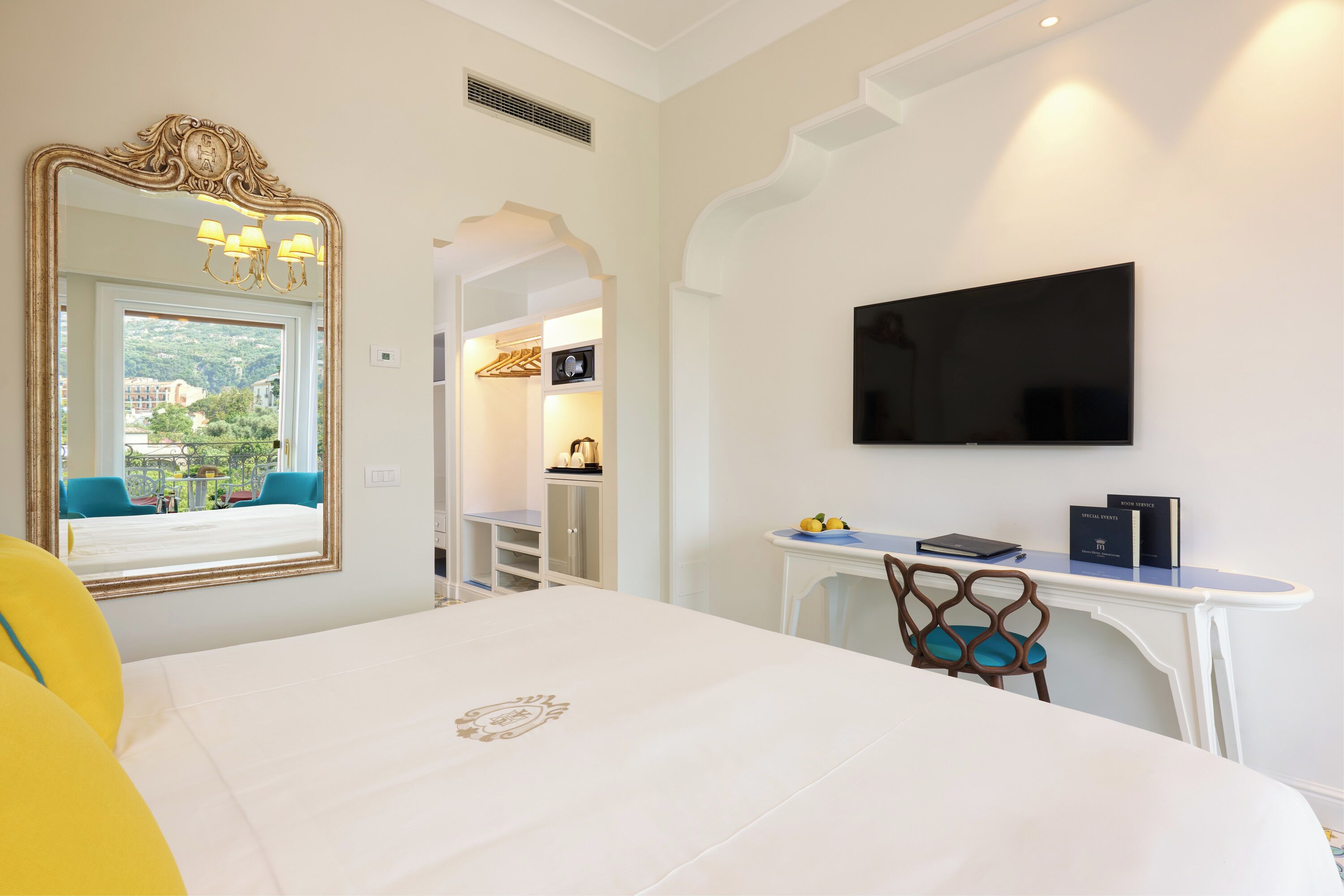 Quarto de hotel com cama, escrivaninha, televisão, espelho e vista para o exterior.