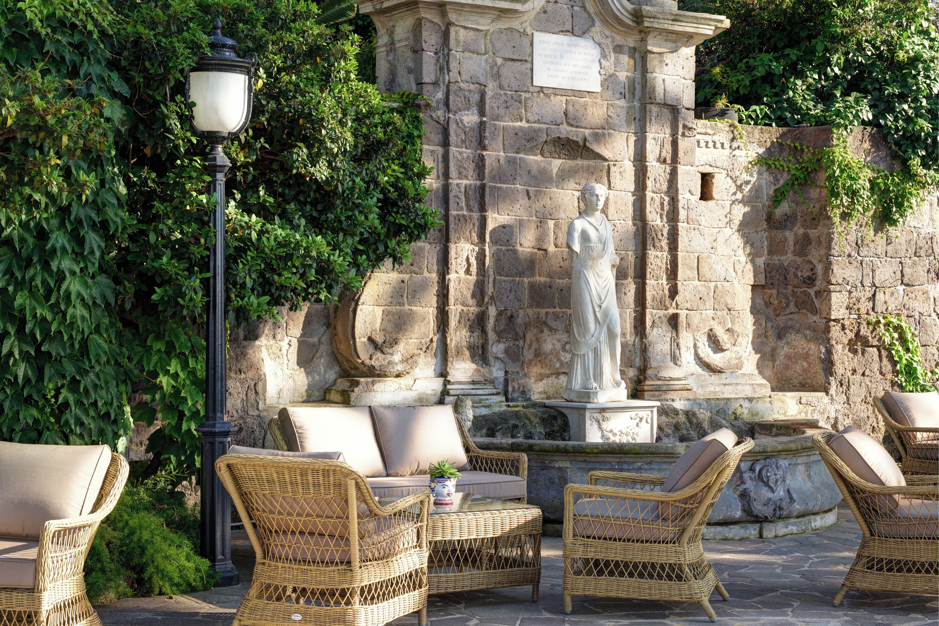 Wicker furniture, a stone wall, and a statue in an outdoor setting.