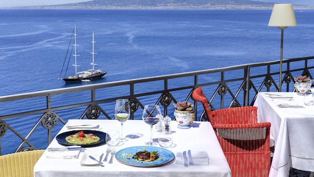 Une table dressée pour le dîner, avec vue sur la mer et une montagne en arrière-plan.