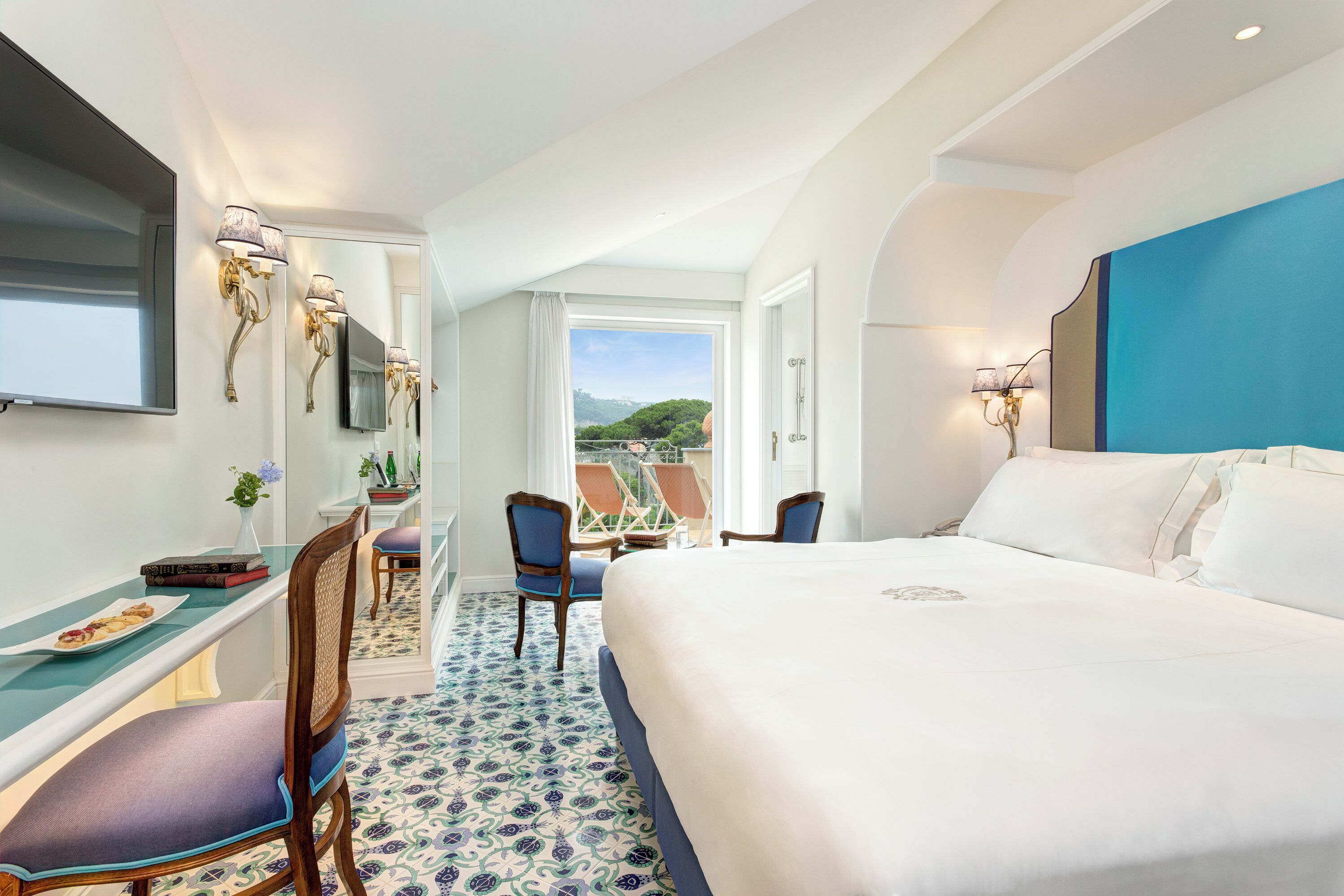 A hotel room with a large bed, a desk with a chair, a TV, and a view of the outdoors.