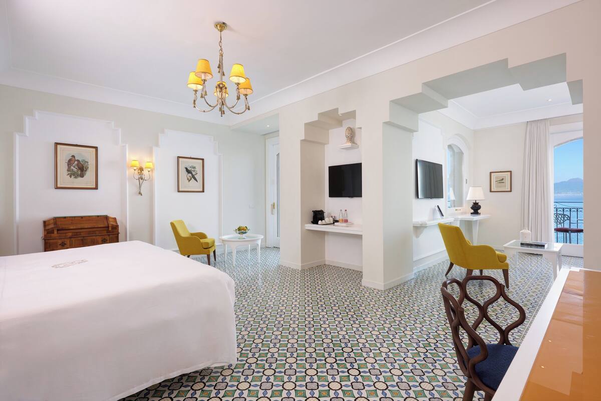 Een hotelkamer met een groot bed, een bureau, een stoel, een televisie en een balkon met uitzicht.