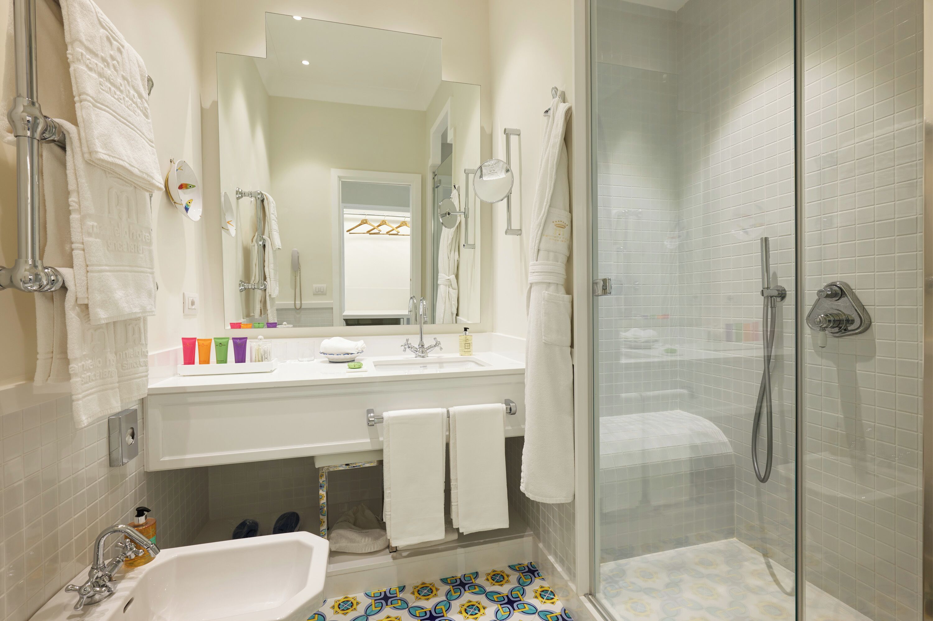 A modern bathroom with a glass shower enclosure, a white sink with a mirror, and a tiled floor.