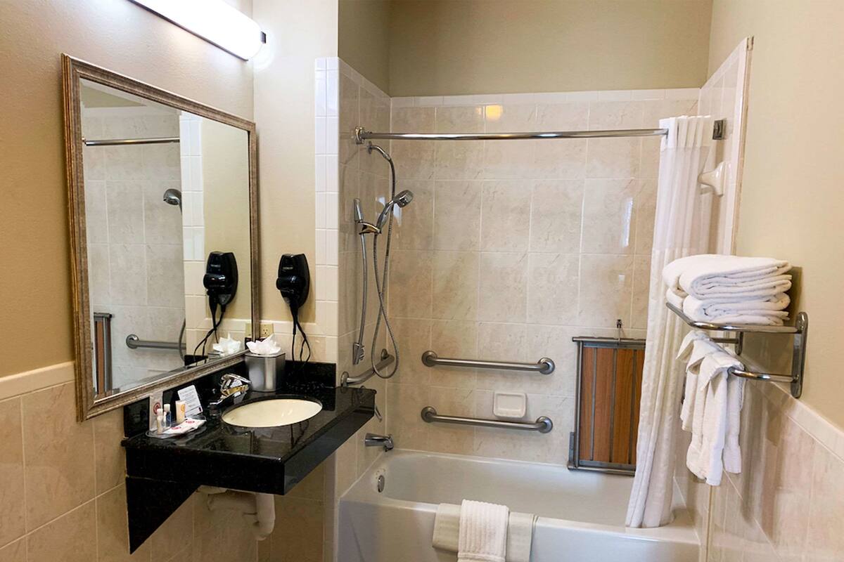 A bathroom with a sink, mirror, shower, and towel rack.