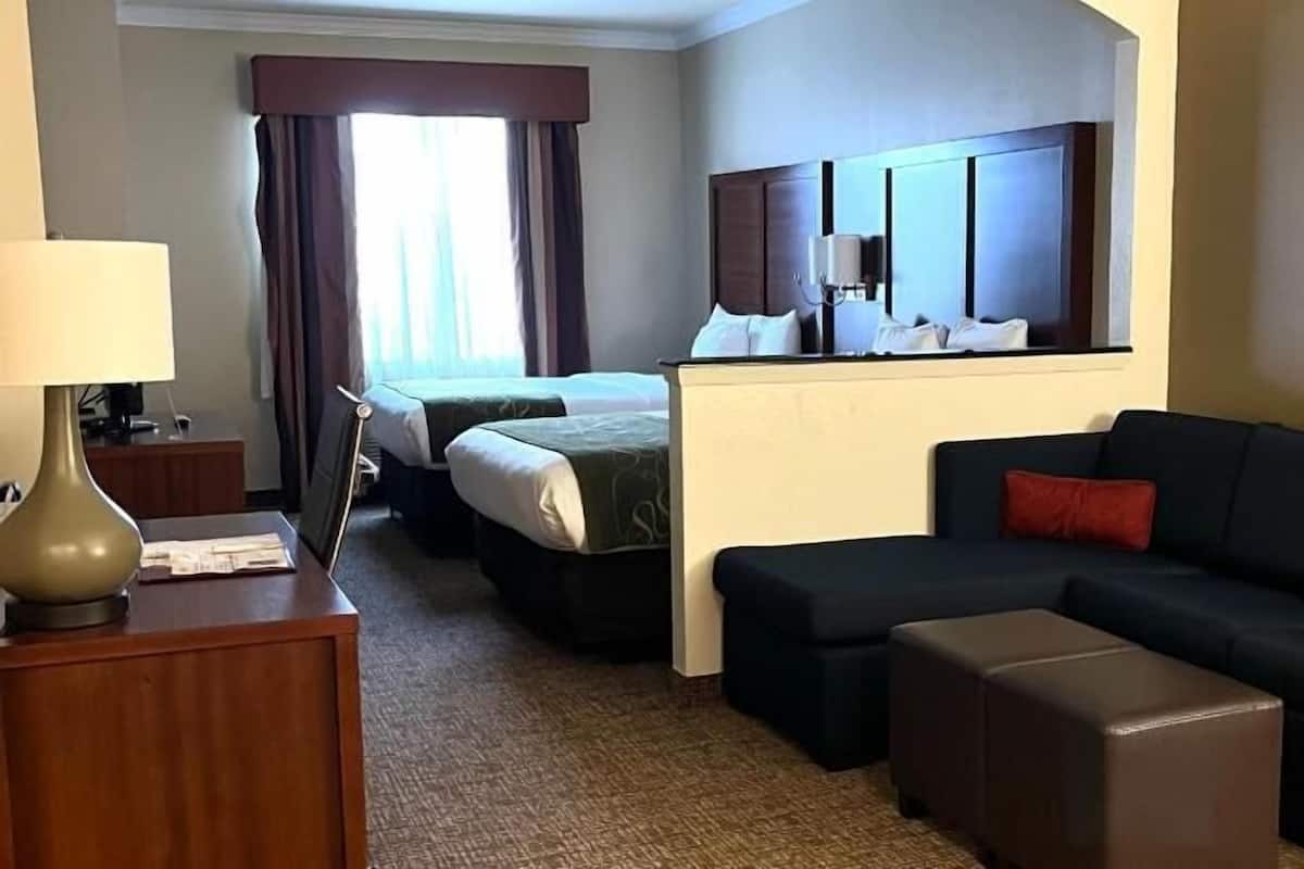 A hotel room with a bed, a sofa, a desk with a lamp, a TV, and a window with curtains.