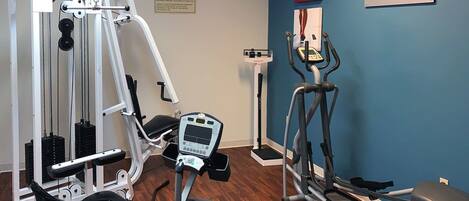 A fitness center with cardio machines, weight training equipment, and a television displaying a fitness program.
