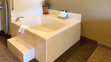 A large, rectangular bathtub with a built-in seat and a small step leading up to it. There is a towel hanging on the wall next to the bathtub.
