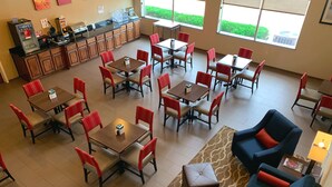 A spacious dining area with multiple tables and chairs, a counter with a coffee machine, and a sofa in the corner.
