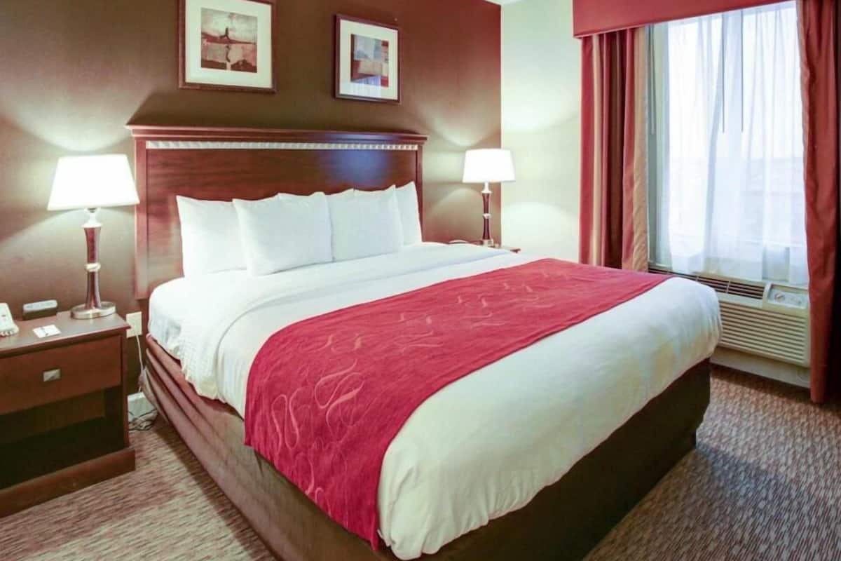 A hotel room with a large bed, two bedside tables with lamps, a window with curtains, and two framed pictures on the wall.