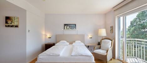 A spacious bedroom with a large bed, a chair, a desk, and a balcony with a railing.