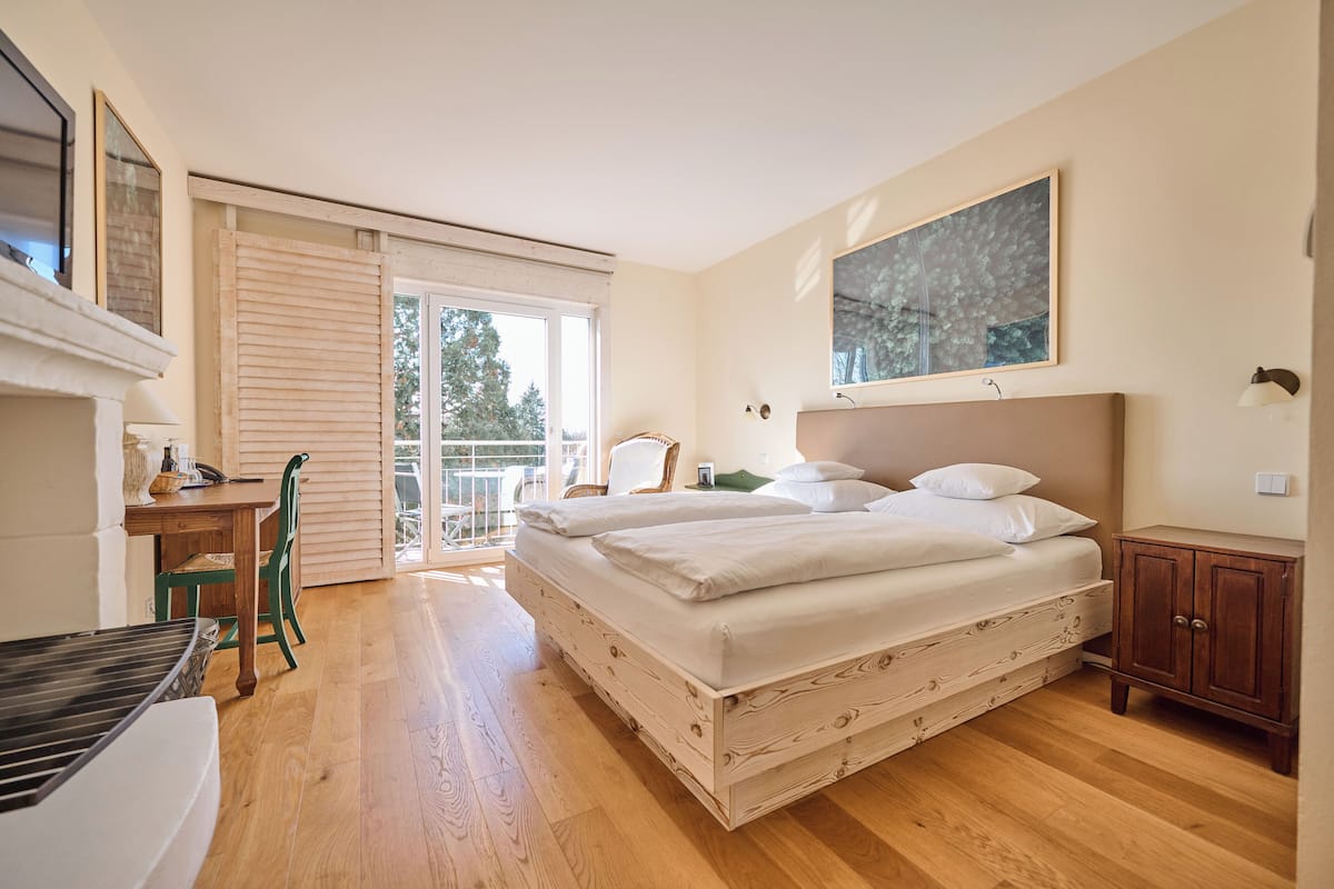 A bedroom with a wooden bed, a desk, a chair, and a view of the outdoors.