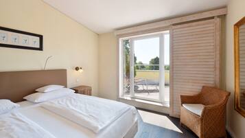 A hotel room with a bed, a chair, a window, and a framed picture on the wall.