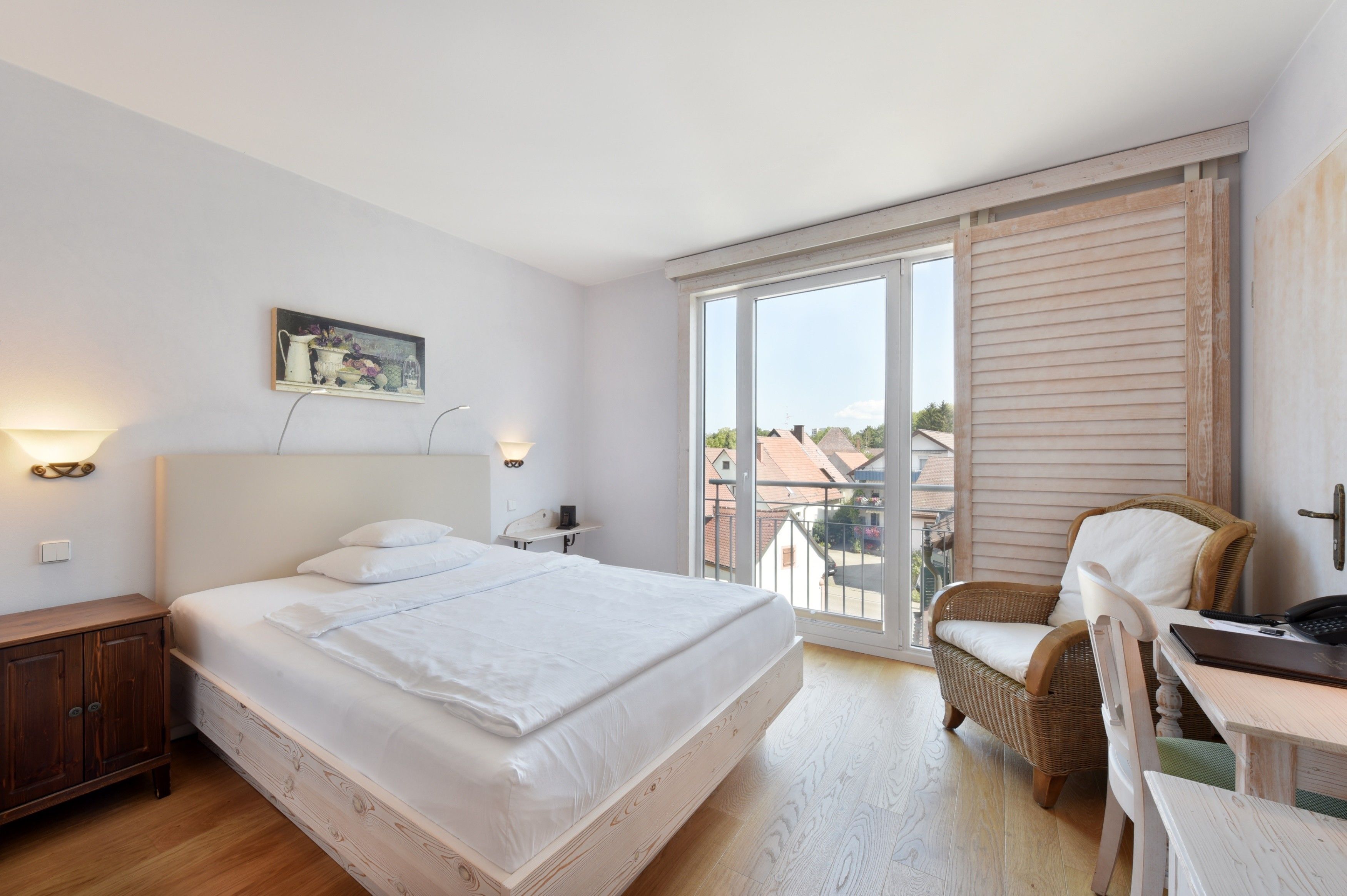 Ein Schlafzimmer mit einem großen Bett, einem Sessel, einem Schreibtisch und Blick ins Freie.