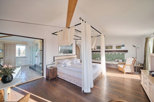 Ein Schlafzimmer mit Himmelbett, Holzboden, großem Spiegel und Blick auf eine grüne Landschaft durch ein Fenster.