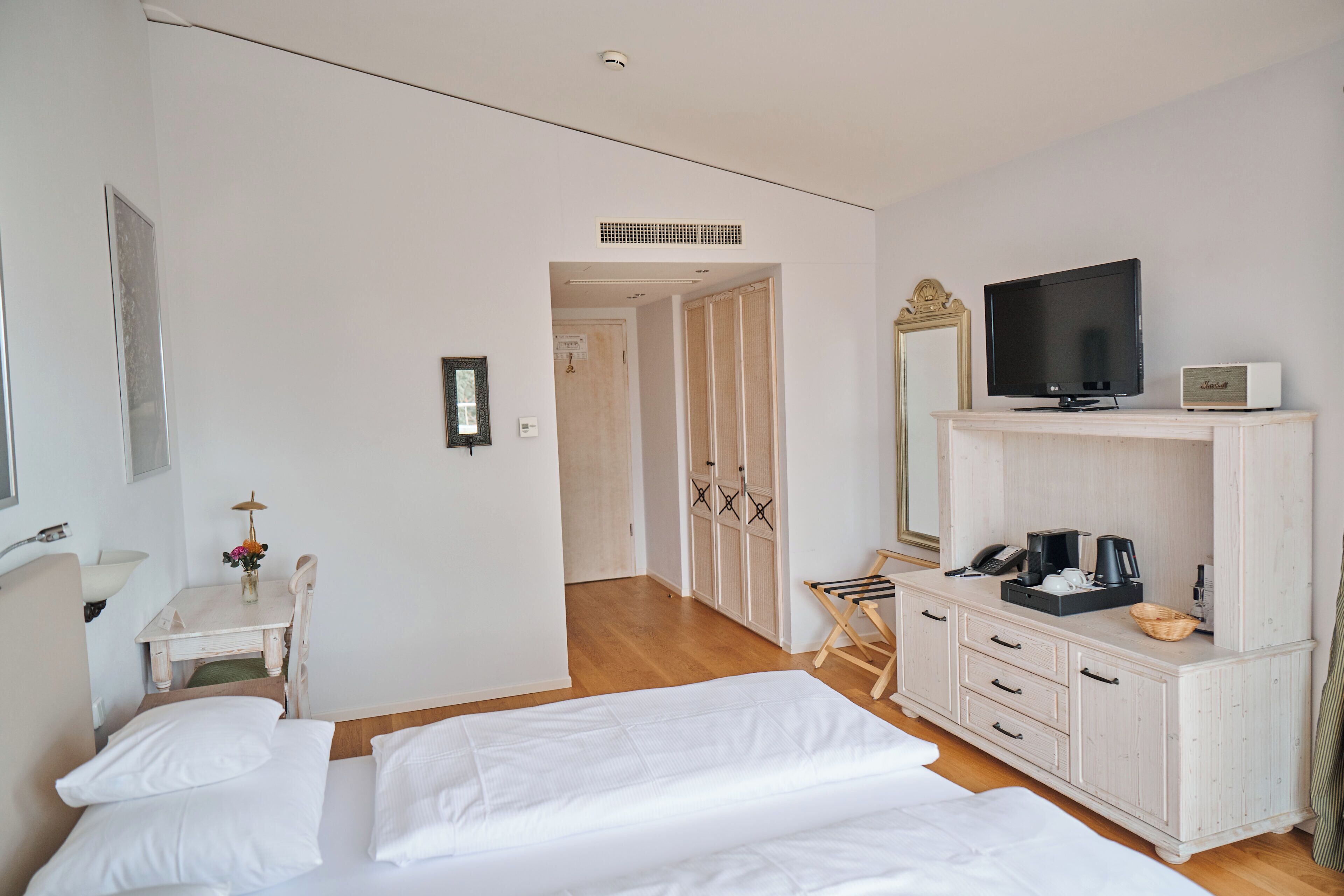 A hotel room with a bed, a TV, a desk with a lamp, and a wardrobe.