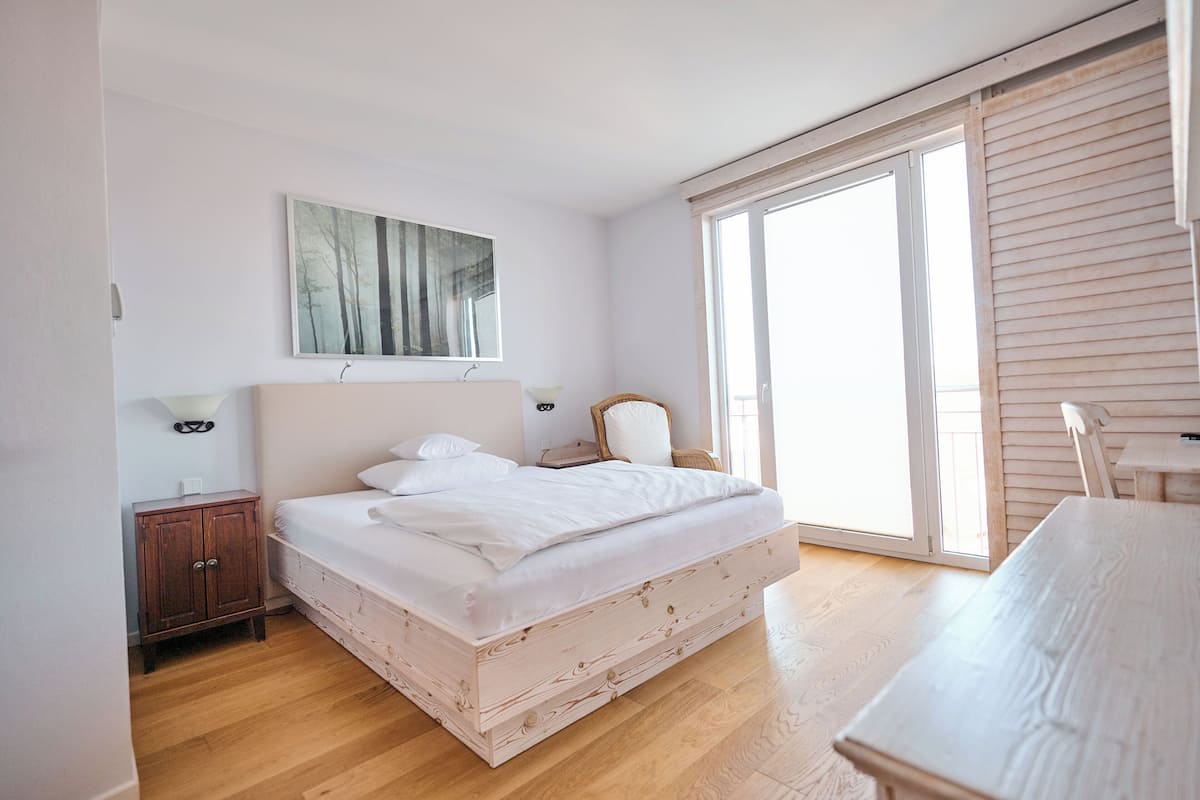 A bedroom with a bed, a nightstand, a chair, a table, and a window.