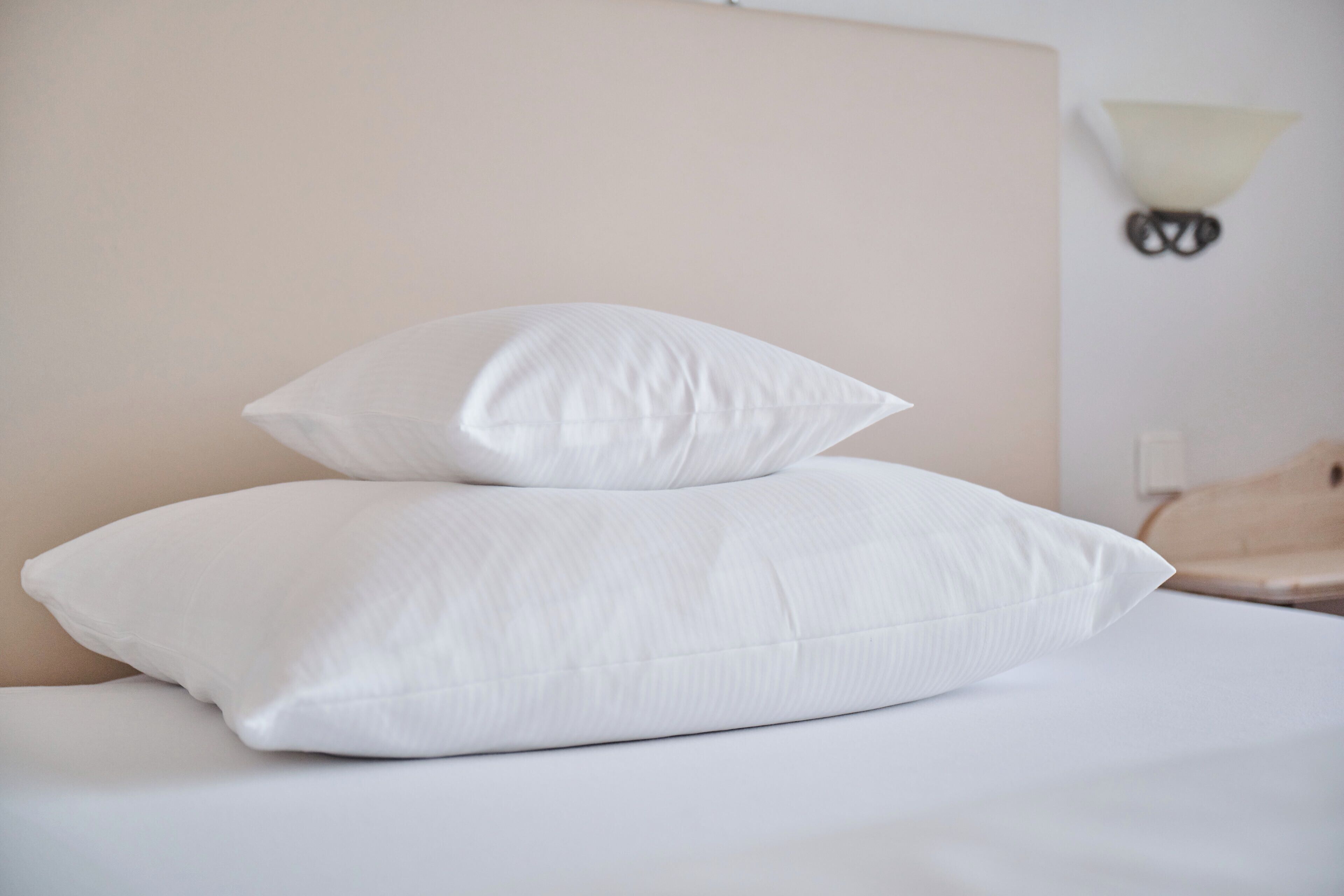 Una cama con dos almohadas blancas y una lámpara fijada a la pared.