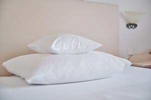 Una cama con dos almohadas blancas y una lámpara fijada a la pared.