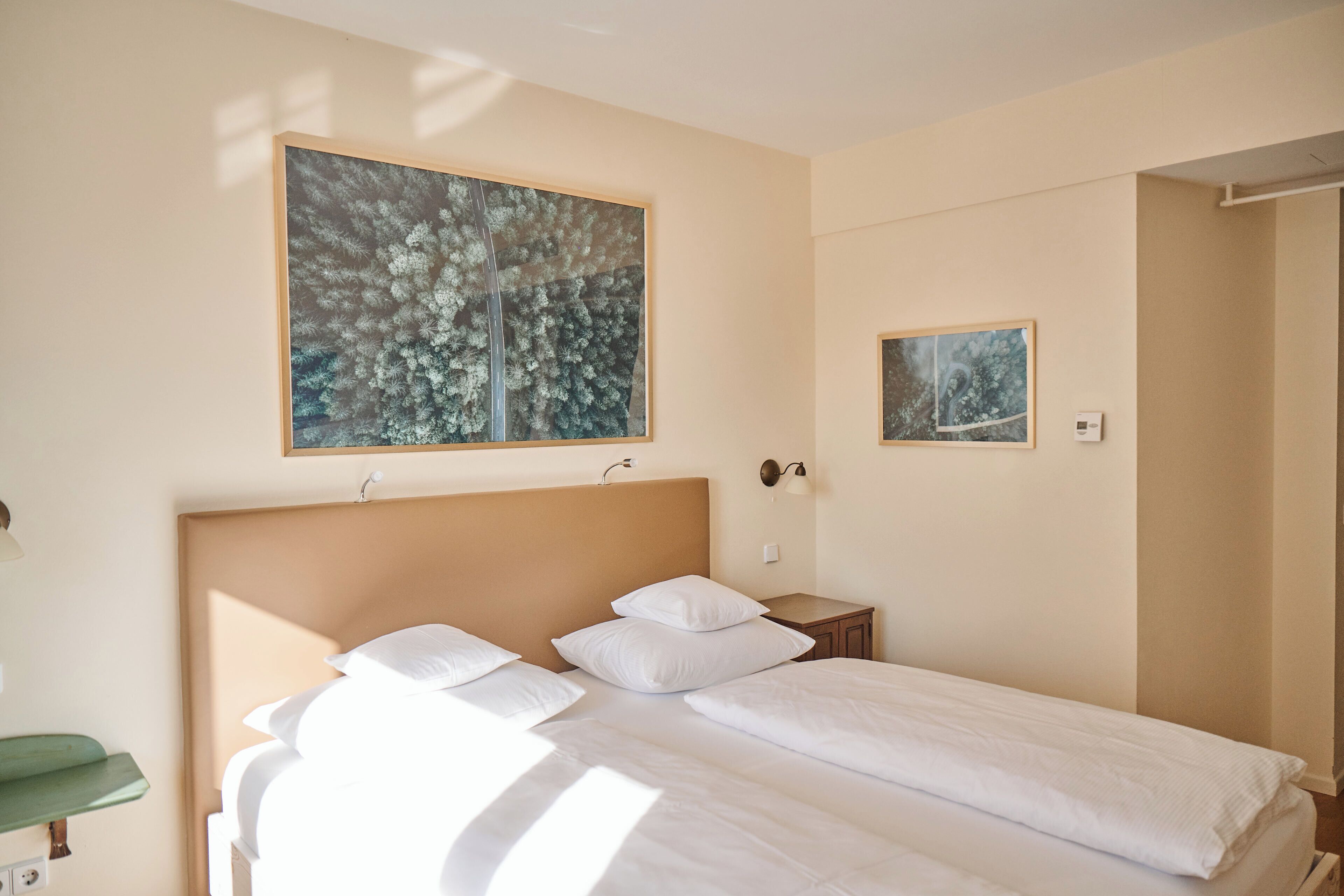 Ein Hotelzimmer mit einem Bett, einem Nachttisch, einer Wandlampe und zwei gerahmten Kunstwerken.