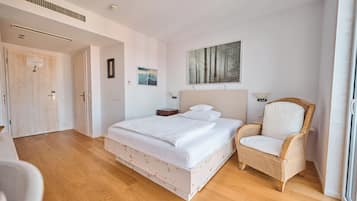 Ein Schlafzimmer mit einem großen Bett, einem Korbstuhl, einem Gemälde und einer Tür.