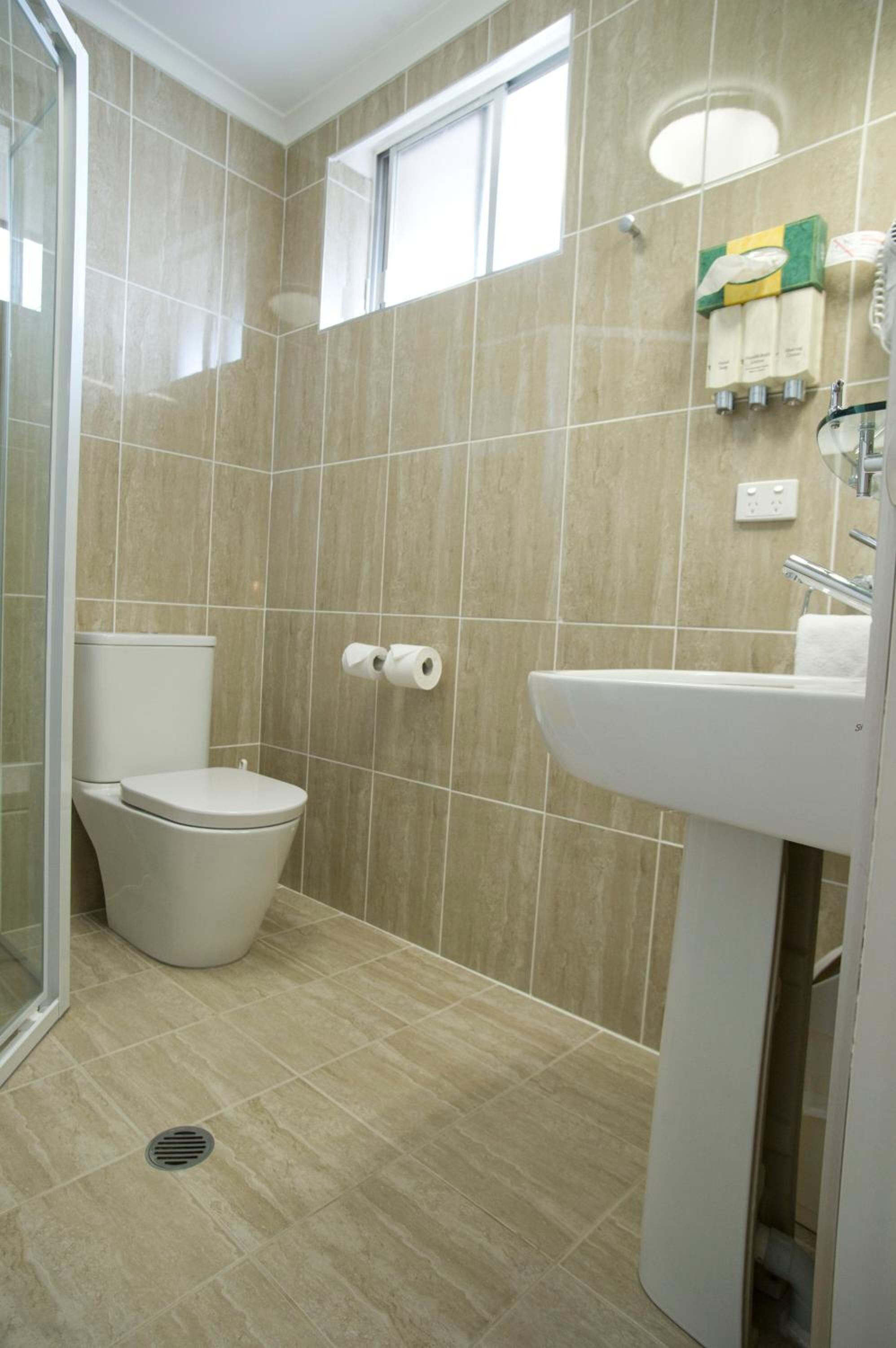 Un baño con azulejos color beige, inodoro, lavamanos y ventana.
