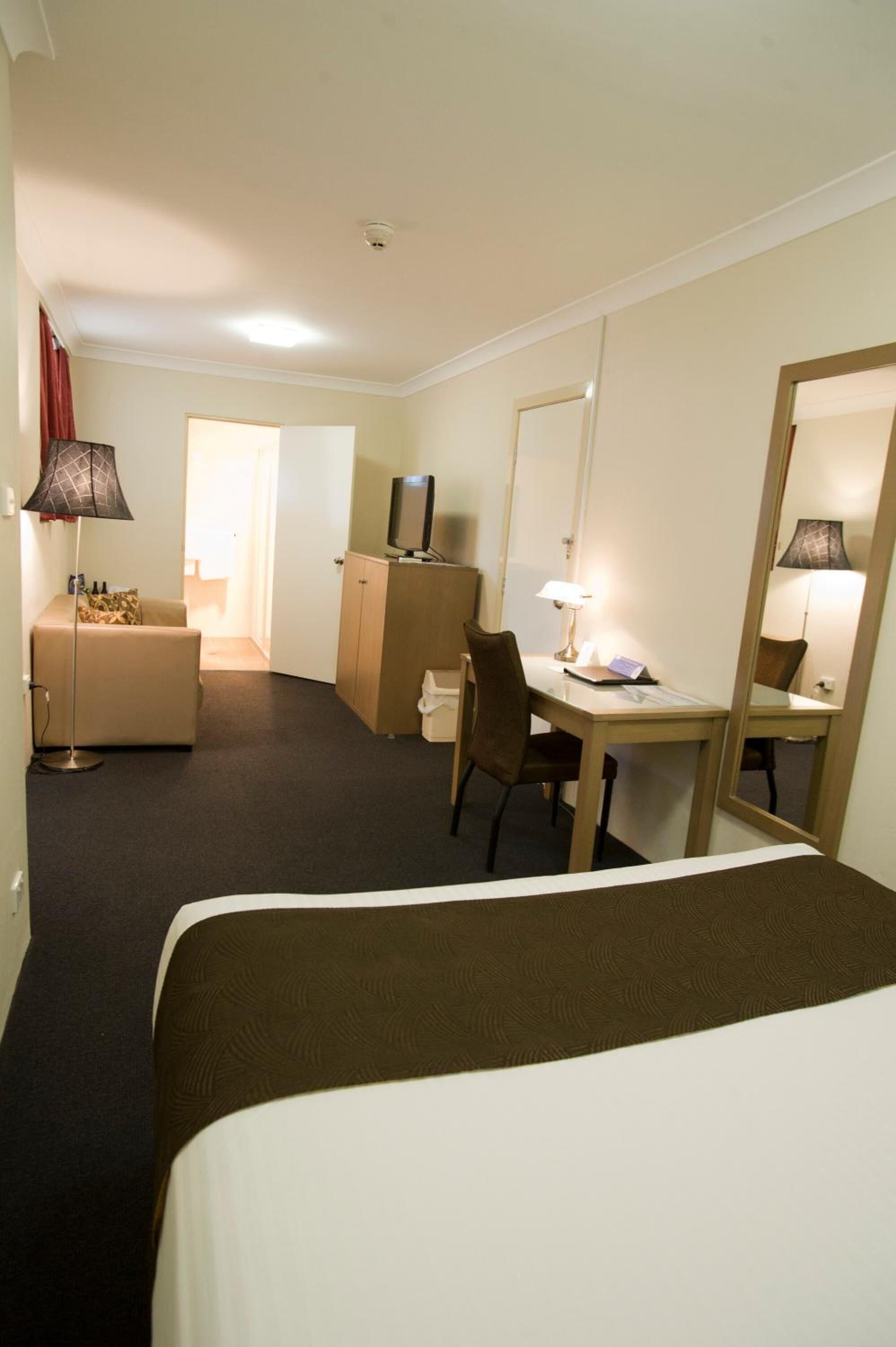 A hotel room with a bed, a desk, a chair, a television, a lamp, and a wardrobe.