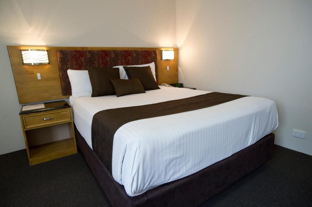 Une chambre d’hôtel avec un grand lit, deux tables de chevet et une tête de lit agrémentée d’un panneau décoratif.