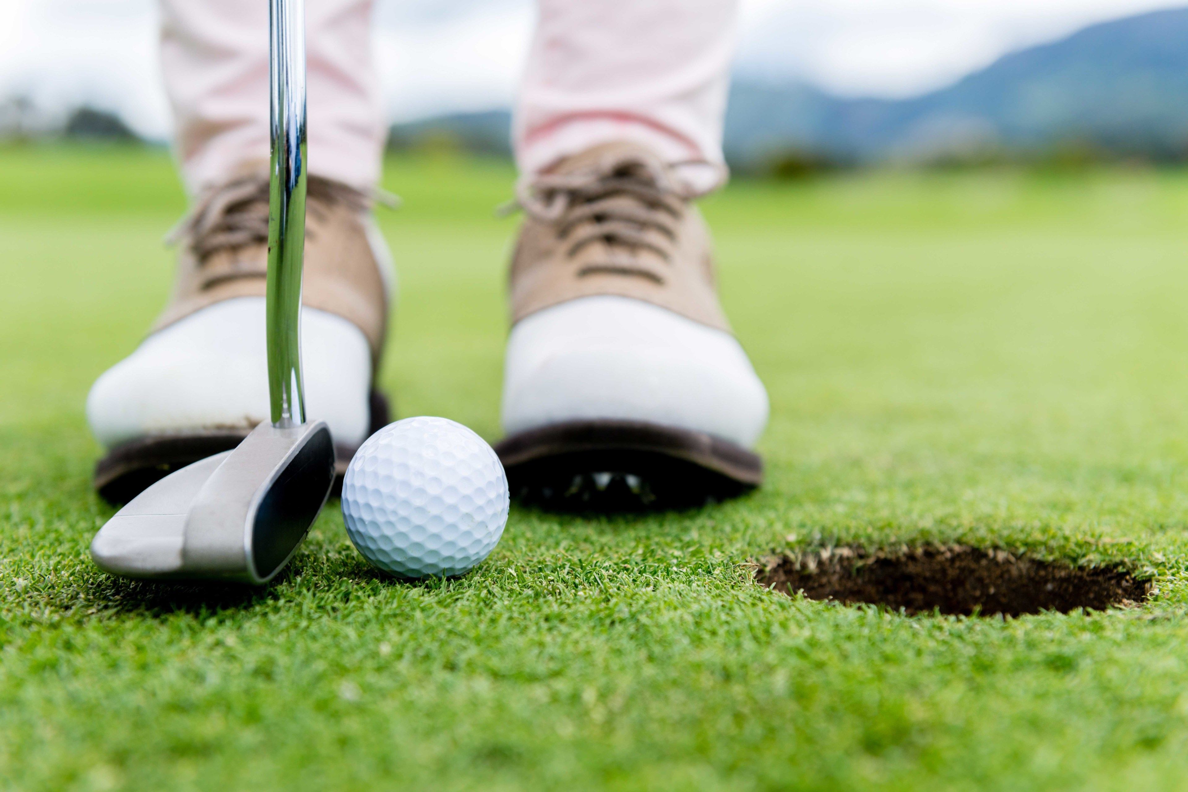 Nærbillede af en golfkølle og bold på grøn græsplæne, med et hul i græsset.