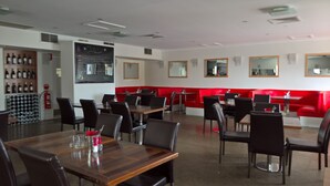 A restaurant with red booths, wooden tables, and black chairs. There are wine bottles on shelves and a chalkboard menu on the wall. - Noah's Mid City Motor Inn (Muswellbrook)