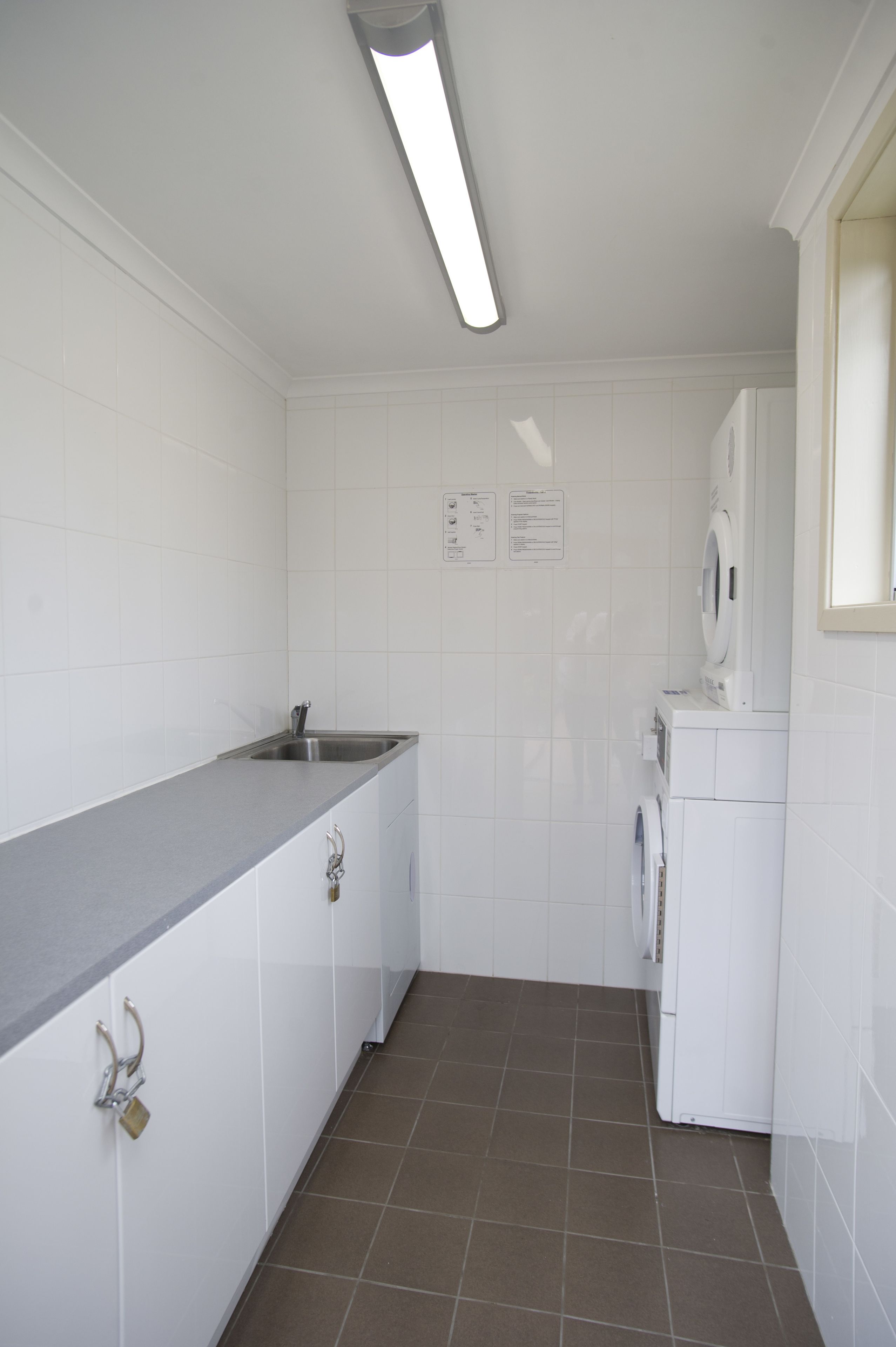 Una cocina compacta con armarios blancos, encimera gris, un lavabo, lavadora y suelo de baldosas.