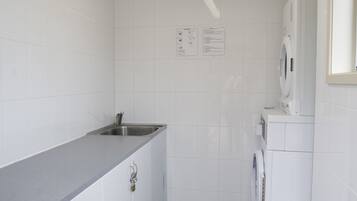 Una cocina compacta con armarios blancos, encimera gris, un lavabo, lavadora y suelo de baldosas.