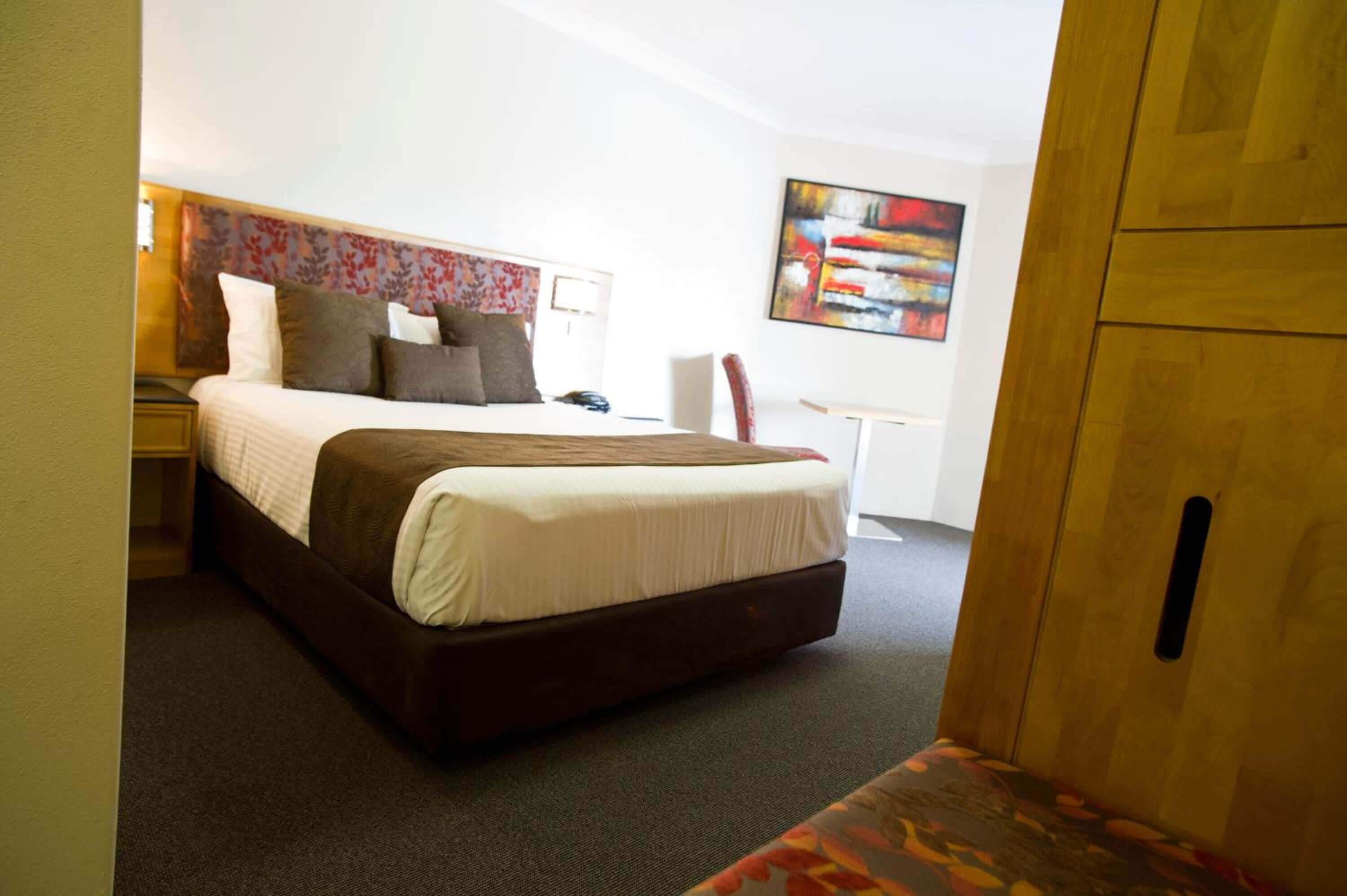 Una habitación de hotel con una cama grande, una mesita de noche, un escritorio y una silla.