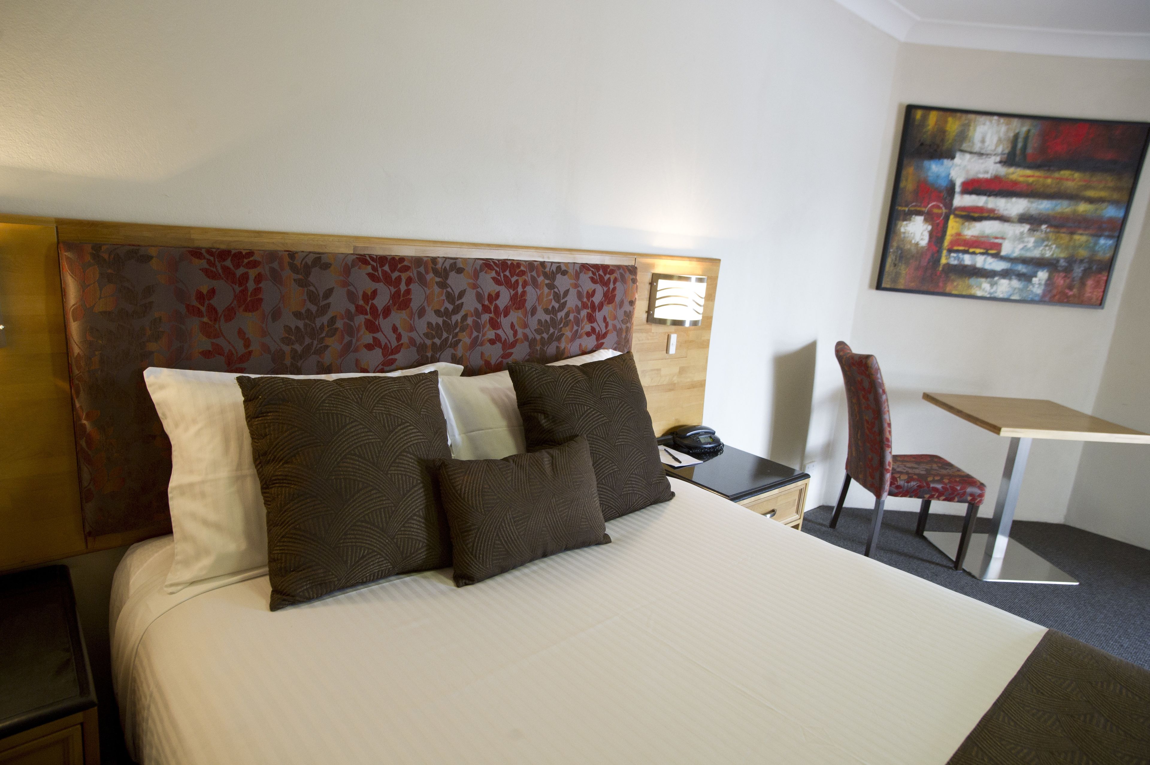 A hotel room with a bed, a desk, a chair, and a painting on the wall.